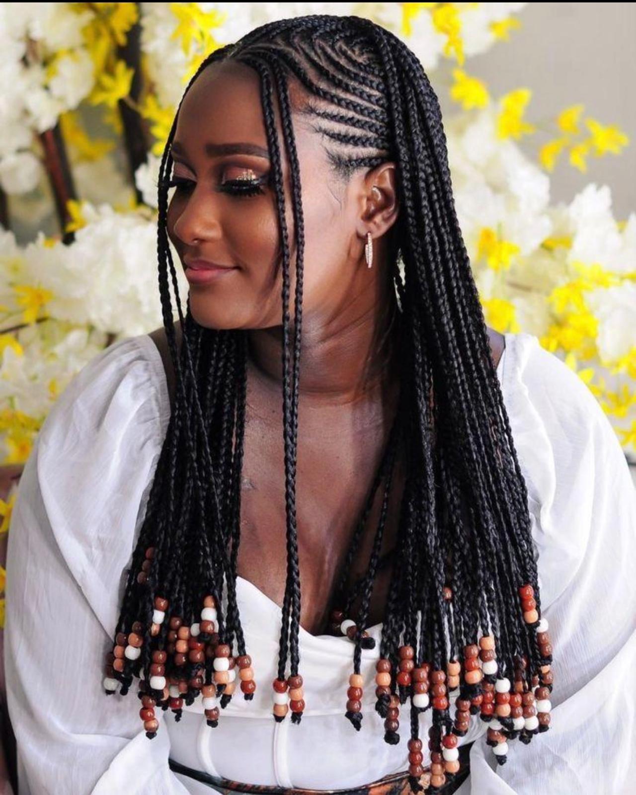 Fulani-inspired tribal braids with lemonade side cornrows and multi-tone wooden beaded ends against a yellow floral wall