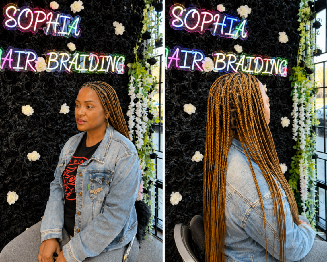 Waist-length copper knotless box braids shown front and side under the salon's colorful neon signage