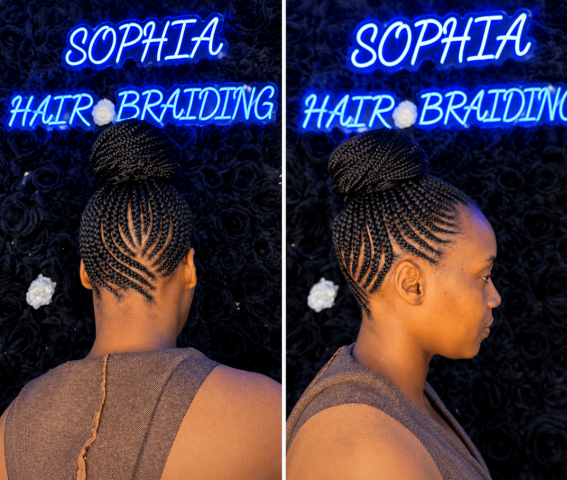 Feed-in stitch cornrows swept into a high braided bun with side profile view under the salon neon sign